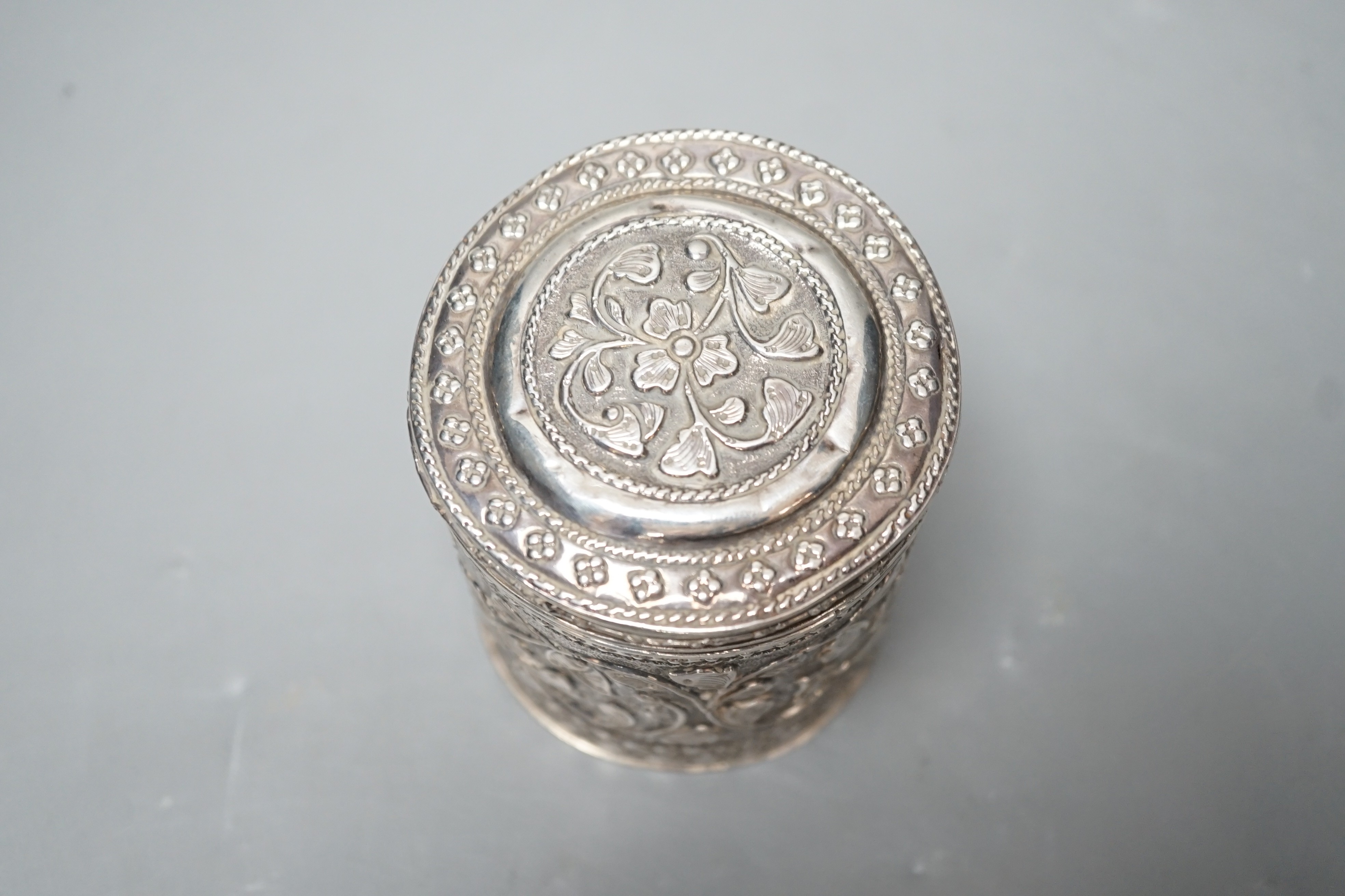 An Indian embossed white metal cigar case, 12.2cm and a similar canister and cover.